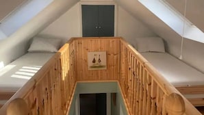 Et værelse med skråvæg, to senge, en trætrappe og en dør.