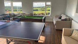 Et værelse med pingpongbord, billardbord og sofa. Der er vinduer med udsigt til grøn bevoksning udenfor.