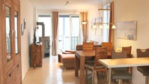 A spacious dining area with a wooden table and chairs, a built-in wood stove, and a balcony with curtains. - Marina View Comfort Stay (Rechlin)