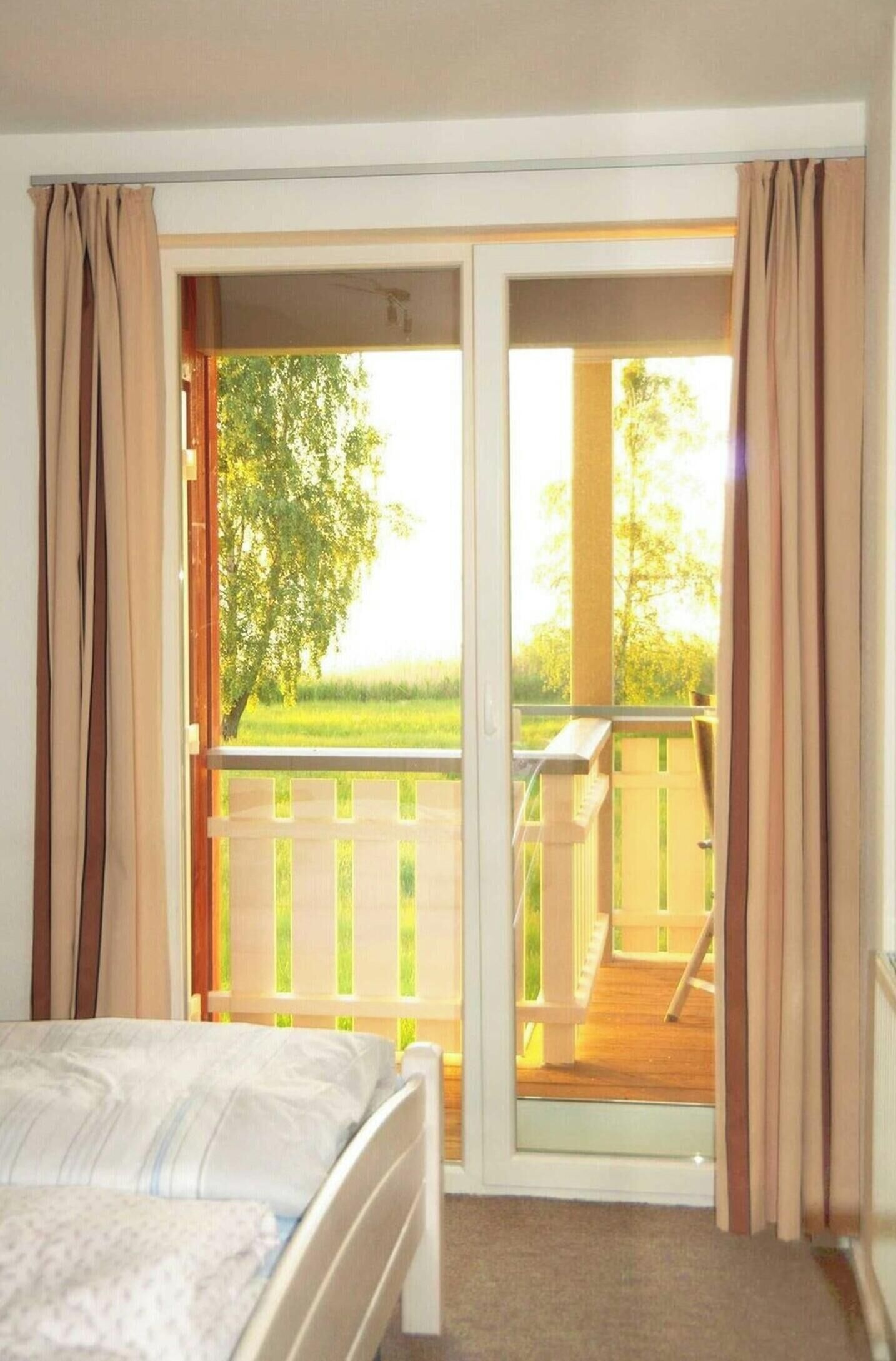 Een slaapkamer met een bed, een schuifdeur naar een balkon met een houten terras en uitzicht op groen.