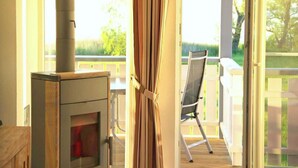 A room with a wood-burning stove, a sliding glass door leading to an outdoor deck, and a chair facing the deck. - Marina View Comfort Stay (Rechlin)