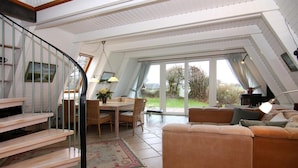 A spacious living area with a staircase, a dining table, and a large window offering a view of the outdoors.