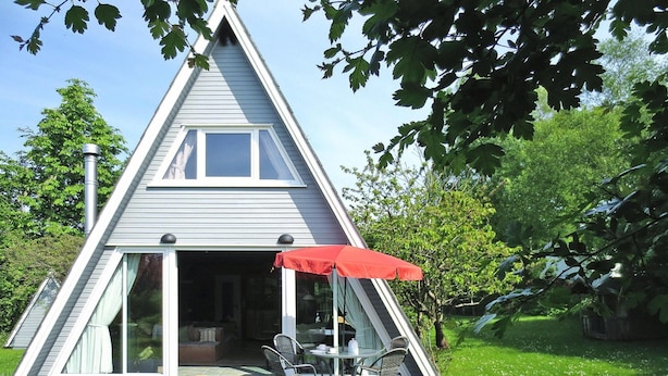 A triangular house with a deck, a dining area with chairs and a table, and a red umbrella.