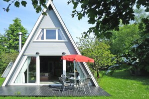 A triangular house with a deck, a dining area with chairs and a table, and a red umbrella. - Ferienhaus Knickkieker Nahe der Ostsee in Damp (Damp)