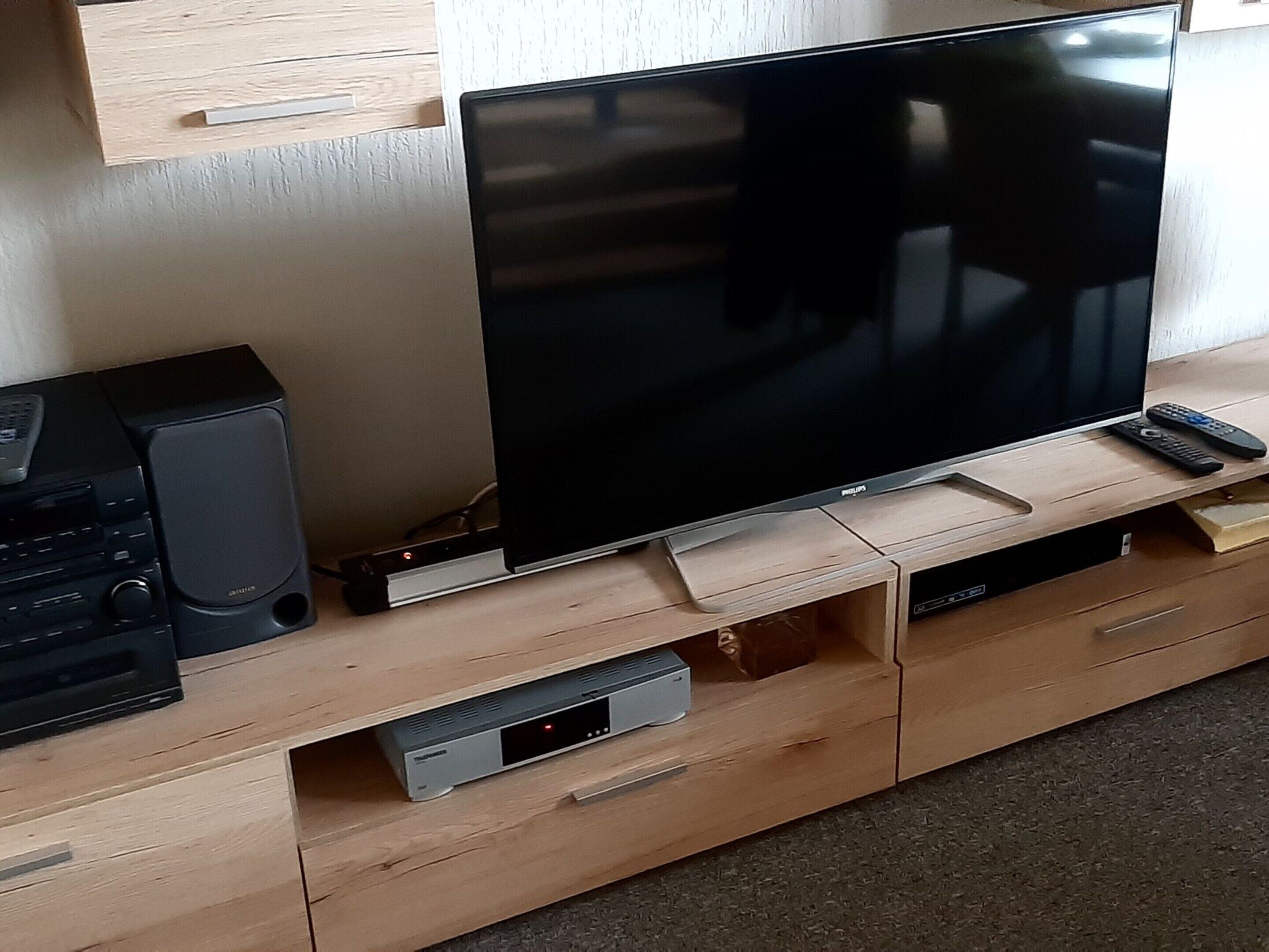 A wooden entertainment center with a flat-screen TV, a soundbar, and a DVD player.