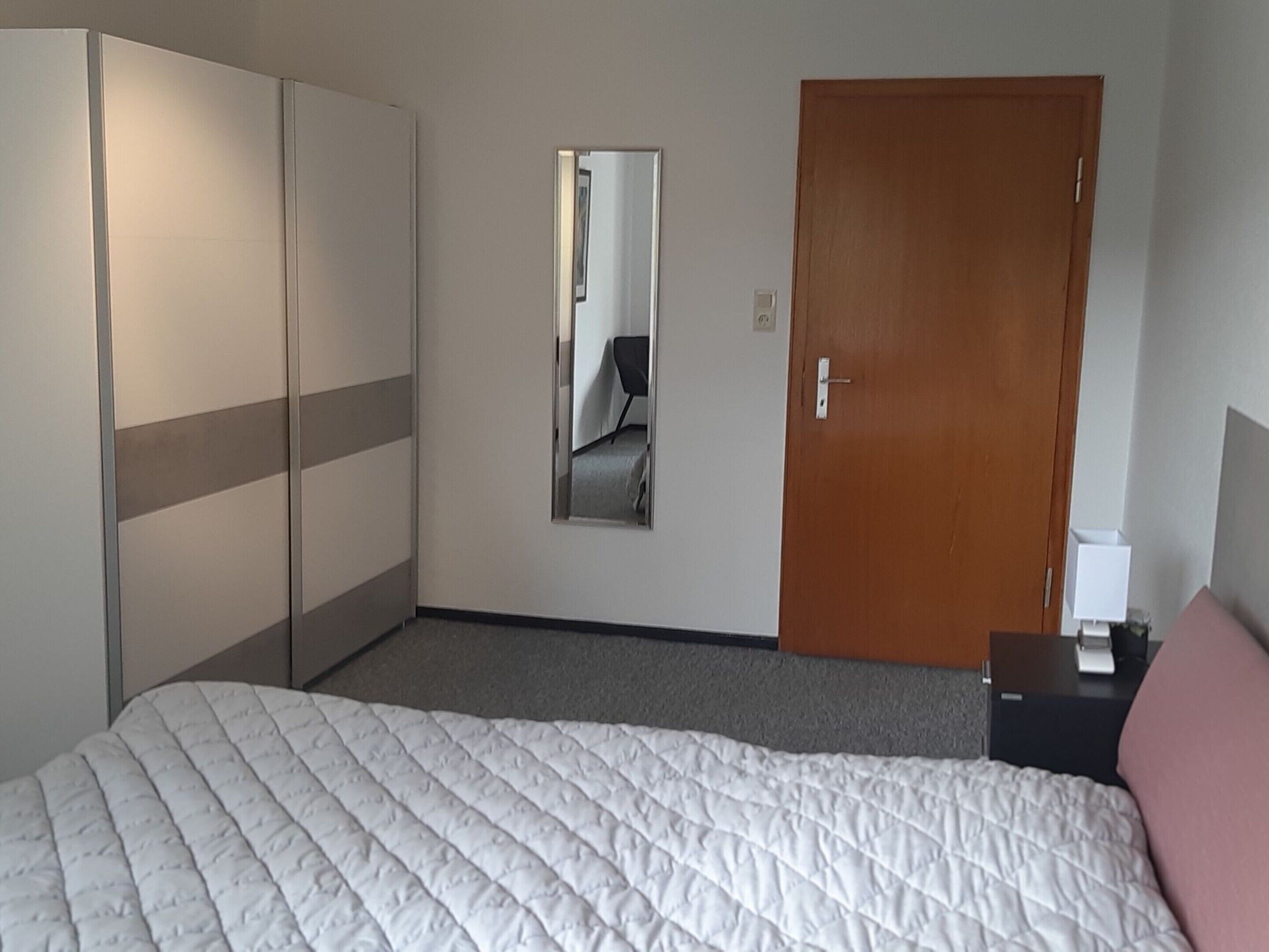 Une chambre d’hôtel avec un lit, une armoire, un miroir et une porte.