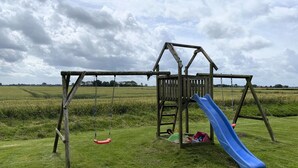 Una estructura de juego de madera con un tobogán en un campo cubierto de césped.