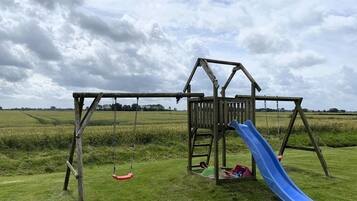 A wooden play structure with a slide in a grassy field.