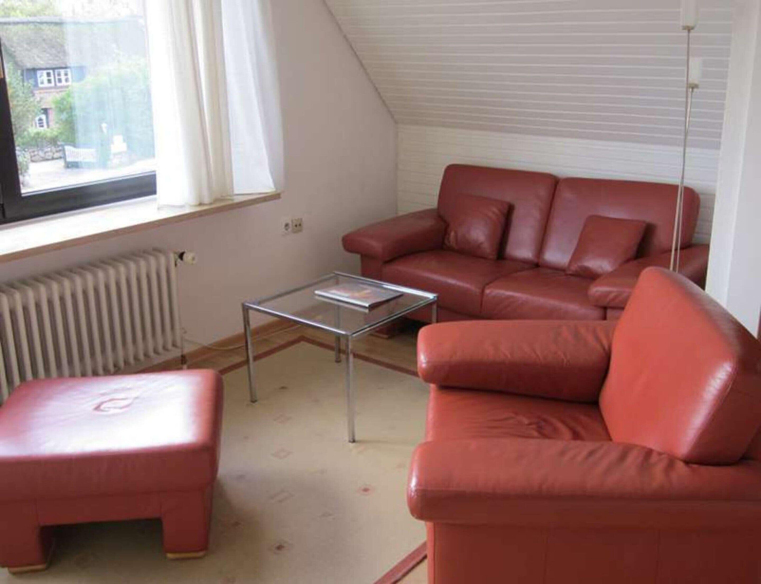 A living room with a red leather sofa, a glass coffee table, and a red ottoman.