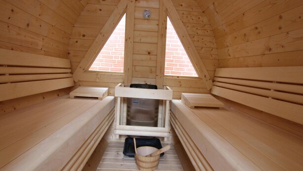 Een houten sauna met banken, waaronder een zitbank, en een klein raam.