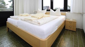 Een hotelkamer met een bed, nachtkastje en een raam met gordijnen.