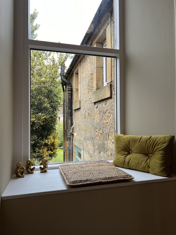 A window seat with a woven mat, a green cushion, and two gold figurines.