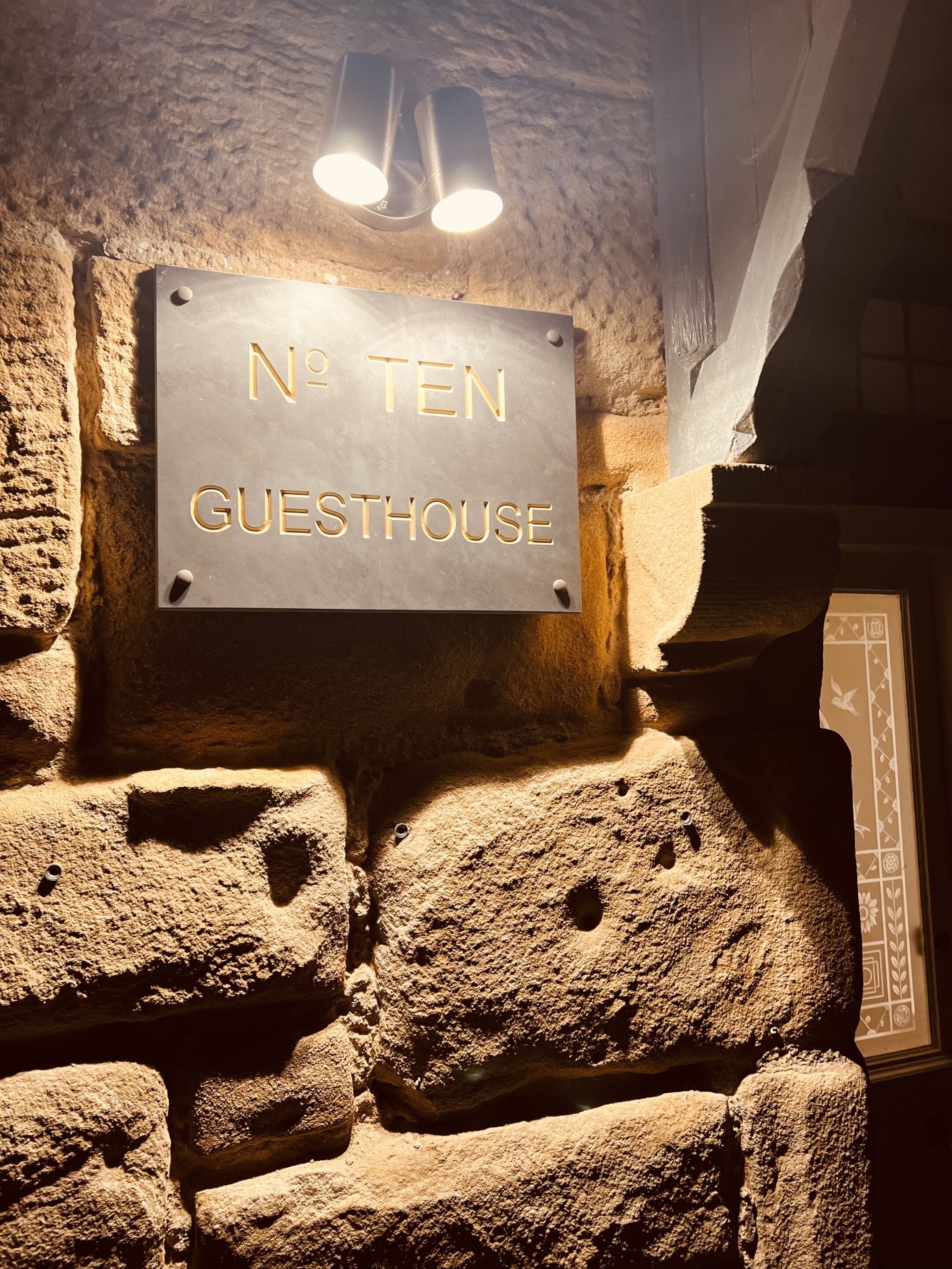 Um muro de pedra com uma placa que diz "Nº Ten Guesthouse".
