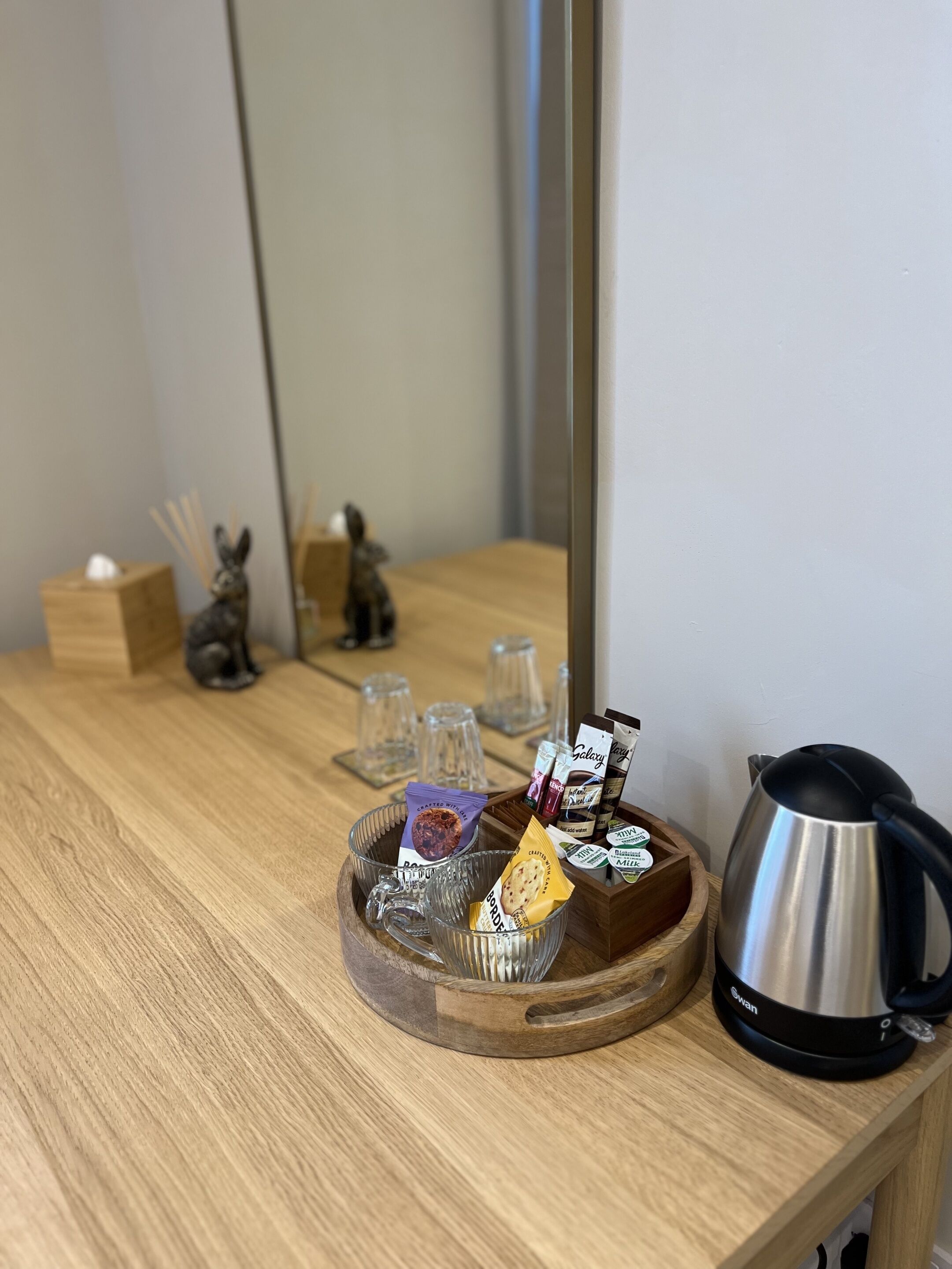 A wooden table with a tray holding tea bags, a kettle, and a small figurine.
