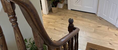 Una escalera de madera que conduce a una habitación con una puerta blanca, un felpudo y una lámpara colgante.