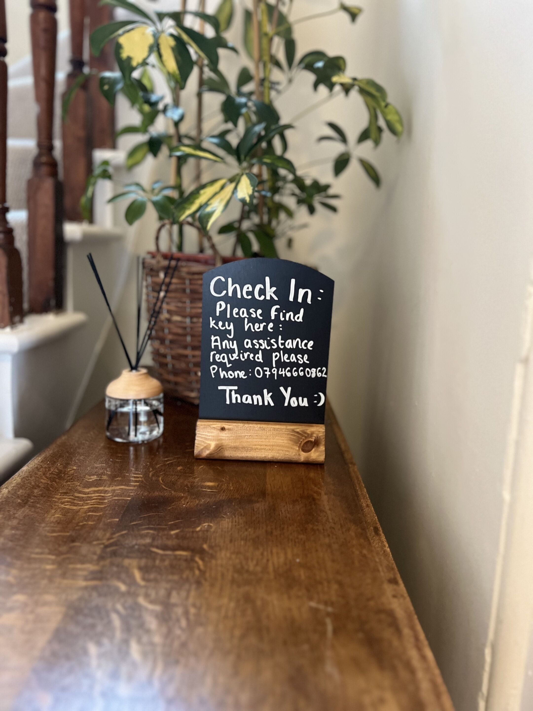 Une table en bois avec une pancarte indiquant : « Enregistrement : veuillez trouver la clé ici. Pour toute assistance, veuillez téléphoner au 07946660962. Merci :) ».