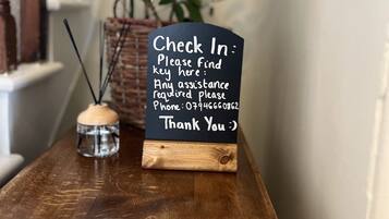 Une table en bois avec une pancarte indiquant : « Enregistrement : veuillez trouver la clé ici. Pour toute assistance, veuillez téléphoner au 07946660962. Merci :) ».