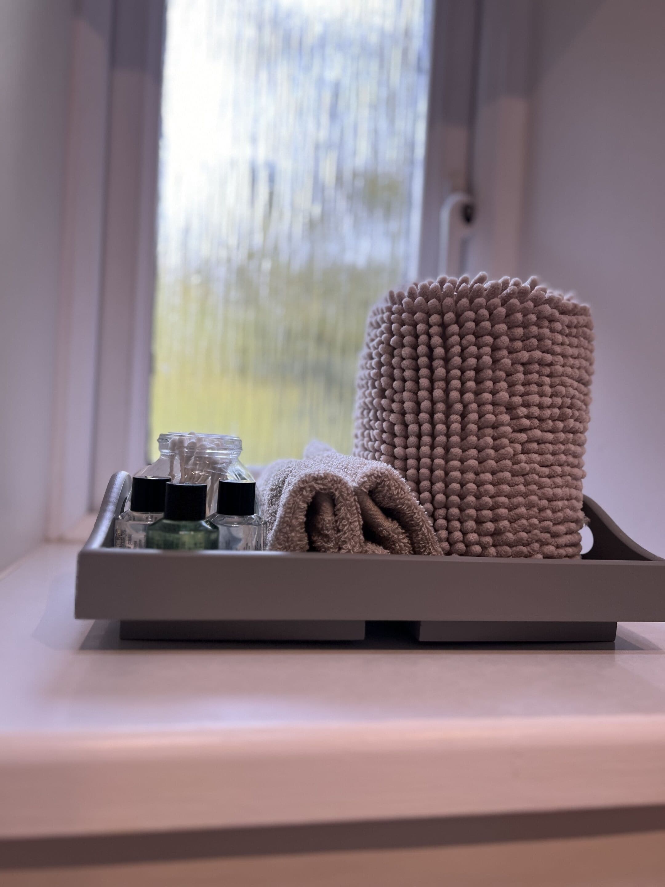 A tray with a rolled towel and toiletries on a windowsill.