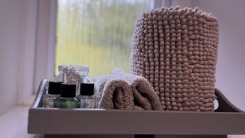 A tray with a rolled towel and toiletries on a windowsill.