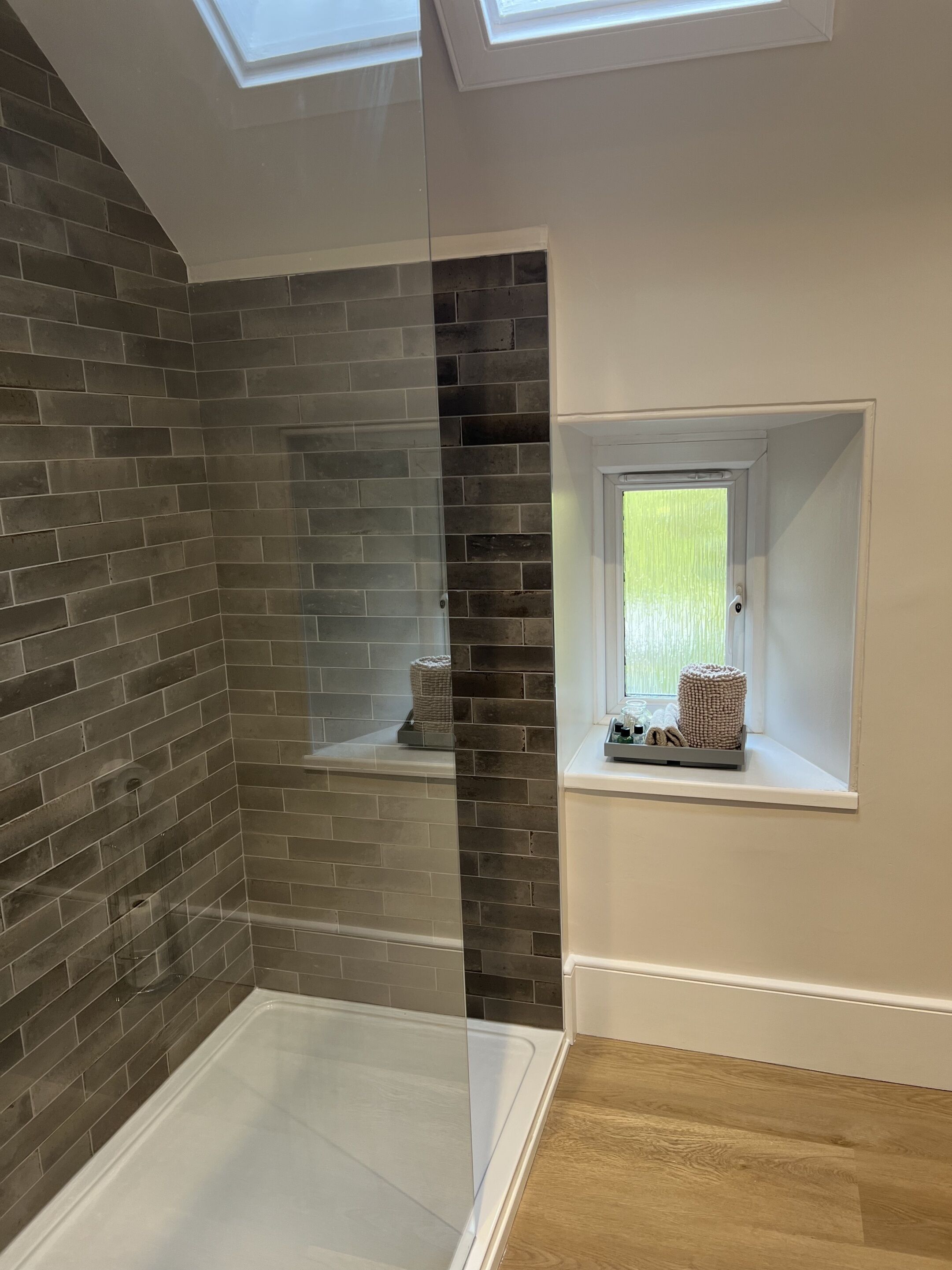Une salle de bain dotée d’une douche à parois de verre, d’une baignoire, d’une fenêtre offrant une vue agréable et d’une étagère contenant des articles de toilette.