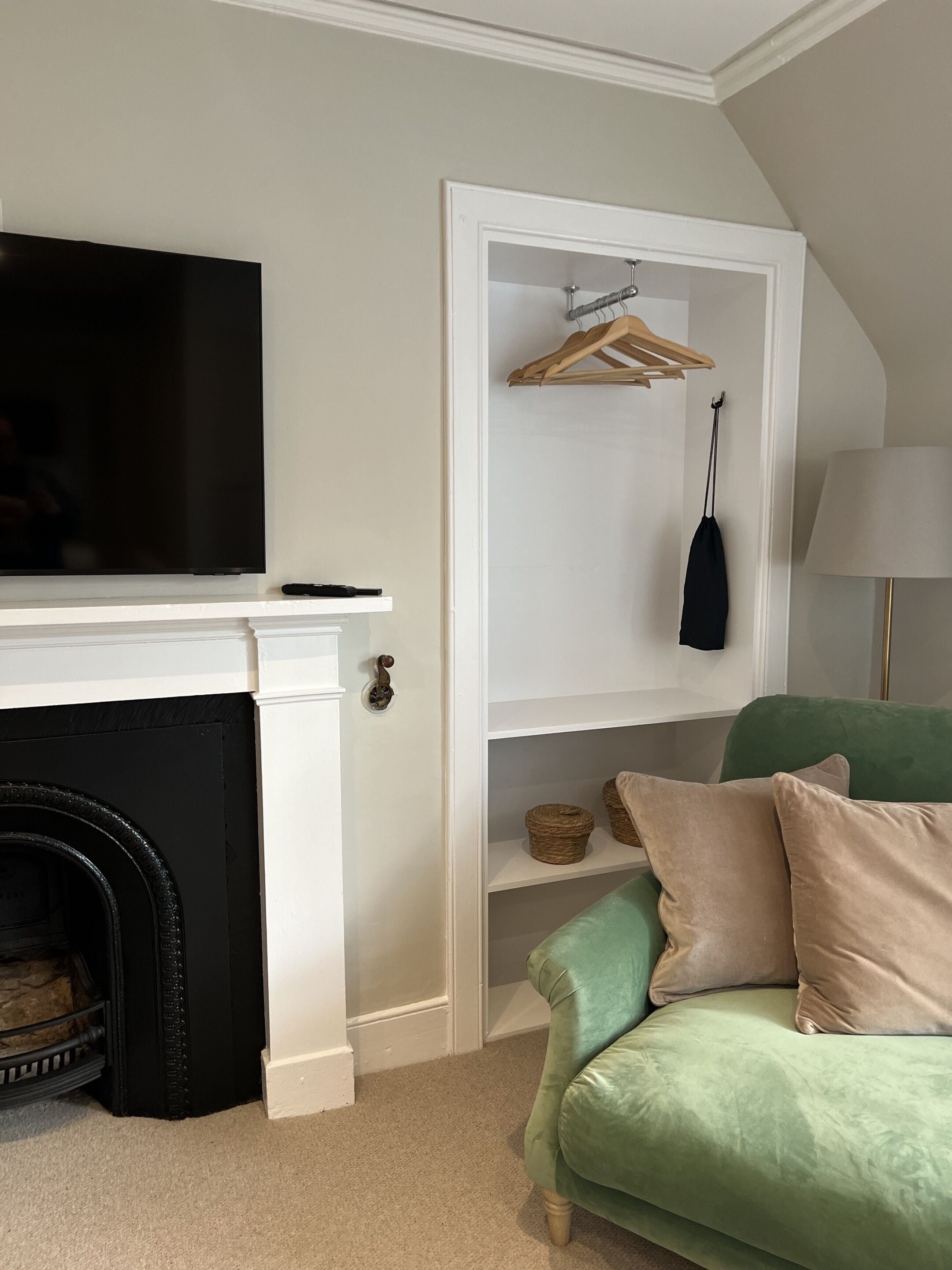 A living room with a fireplace, a television, a green sofa, a lamp, and a wooden wardrobe.