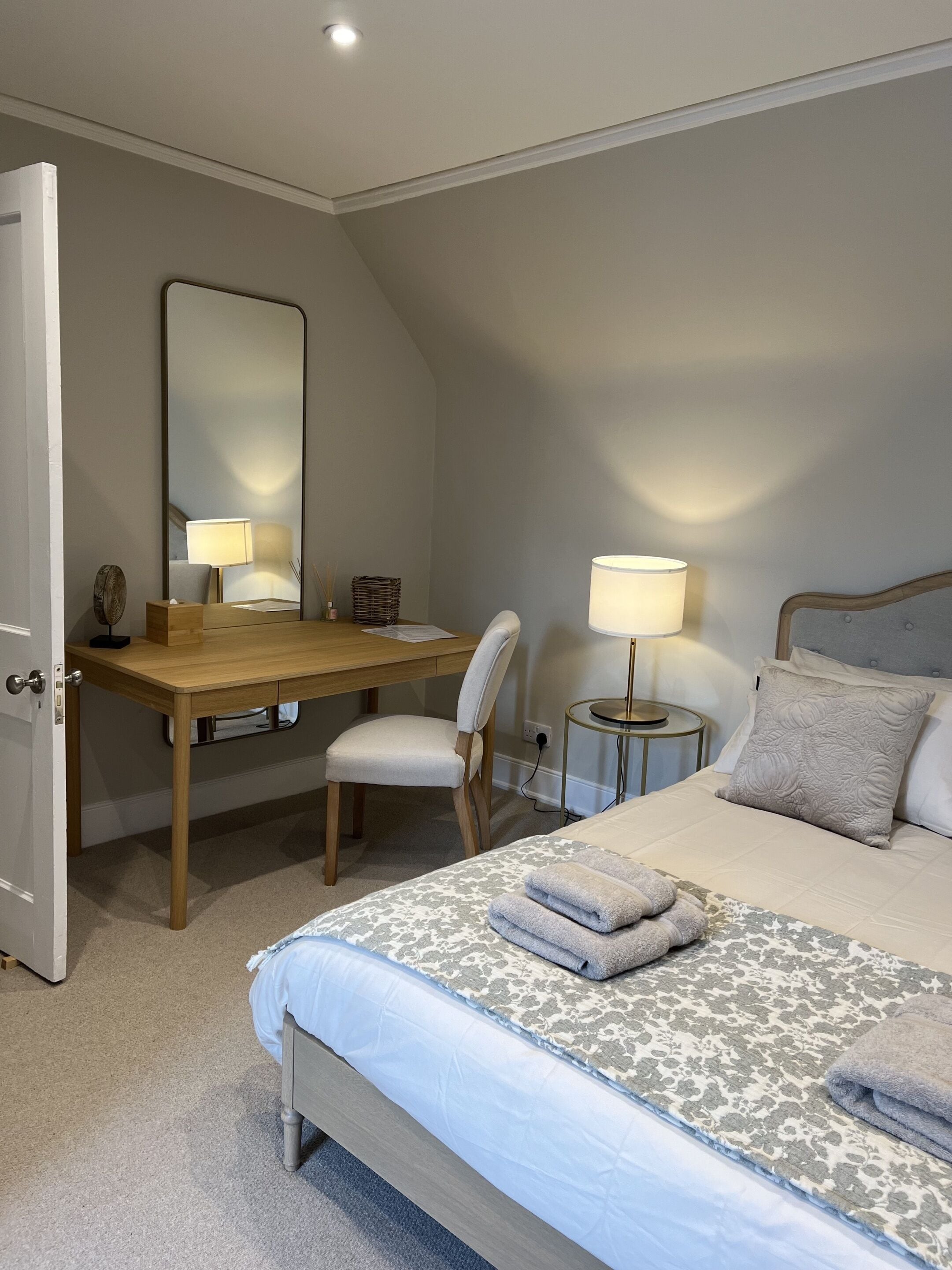 Un dormitorio con cama, escritorio, silla, mesita de noche y espejo.