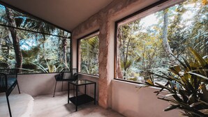 Habitació amb grans finestres, una cadira negra i una taula petita.
