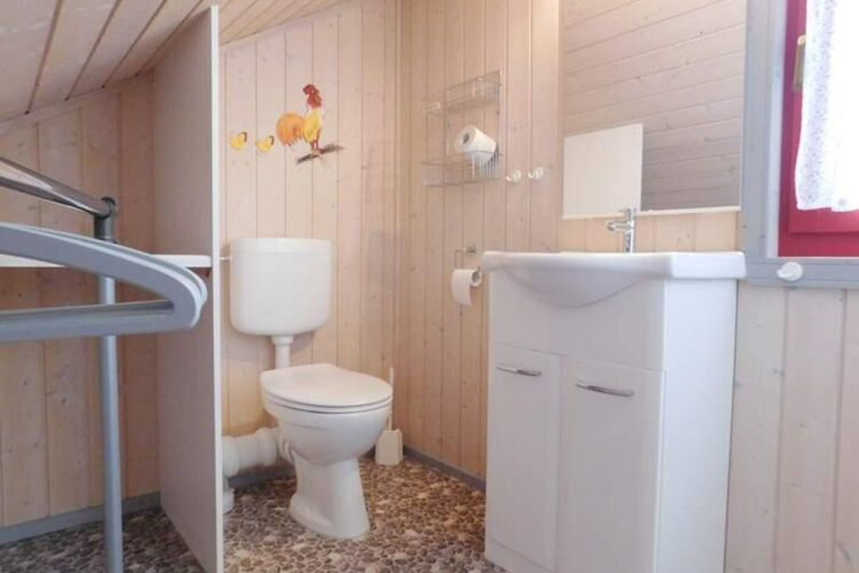 Une salle de bain aux murs lambrissés, équipée de toilettes, d’un lavabo et d’un miroir.