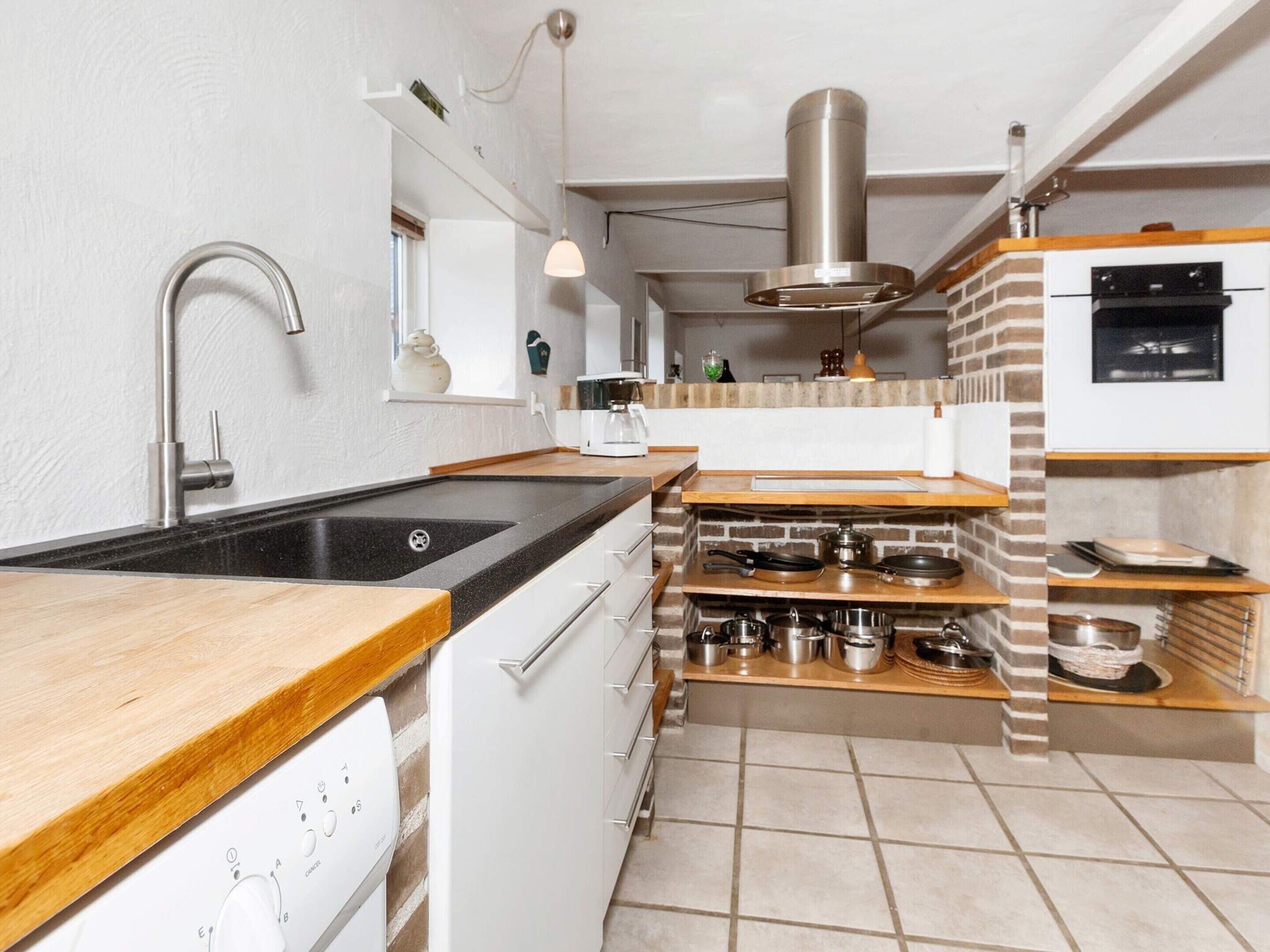Una cocina moderna con encimera negra, electrodomésticos de acero inoxidable y una pared de ladrillo decorativa.