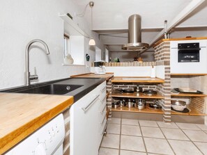 A modern kitchen with a black countertop, stainless steel appliances, and a brick accent wall. - 4 Star Holiday Home in Frederikshavn (Frederikshavn)