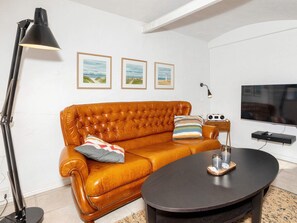 Ett vardagsrum med en soffa i läder, ett runt soffbord, en golvlampa, en tv och inramade tavlor på väggen.