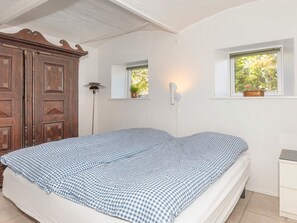 A bedroom with a bed, a wardrobe, a bedside lamp, and a window with a view of trees. - 4 Star Holiday Home in Frederikshavn (Frederikshavn)
