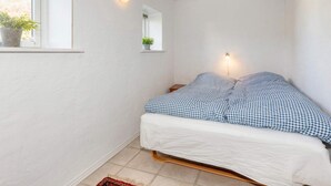 A small bedroom with a single bed, a window with a plant, and a wall-mounted light fixture. - 4 Star Holiday Home in Frederikshavn (Frederikshavn)