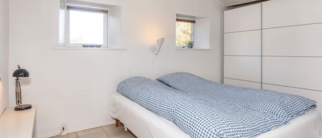 A bedroom with a bed, two windows, a desk with a lamp, and a wardrobe.