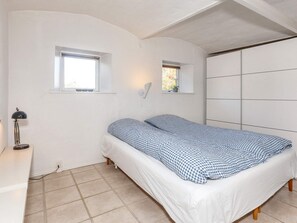 A bedroom with a bed, two windows, a desk with a lamp, and a wardrobe. - 4 Star Holiday Home in Frederikshavn (Frederikshavn)