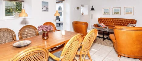 A dining area with a wooden table and wicker chairs, a sofa, and a floor lamp.