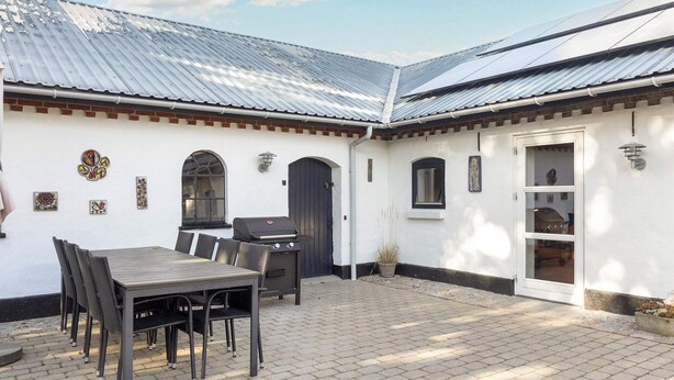 A patio with a table and chairs, a grill, and a door with a window. - 4 Star Holiday Home in Frederikshavn (Frederikshavn)