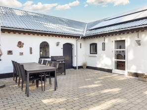Eine Terrasse mit Tisch, Stühlen, einem Grill und einer Tür mit Fenster.