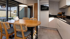 A modern kitchen with a dining area, including a wooden table and chairs, a built-in oven, and a large window. - Docklodge at Frisian Lakes With Private Mooring (Delfstrahuizen)