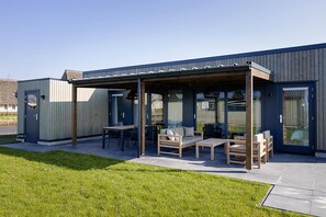 Un bâtiment moderne doté d’un patio couvert, aménagé avec du mobilier d’extérieur et une table.