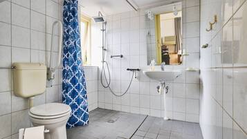 A bathroom with a toilet, shower, sink, and a mirror.