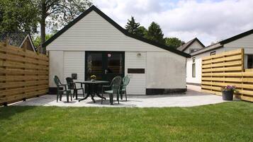 A white building with a pitched roof, a patio with a table and chairs, and a wooden fence.