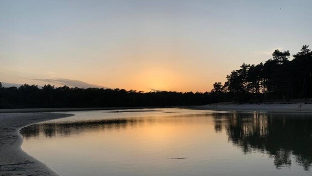 Un lago tranquillo al tramonto con una riva boscosa.