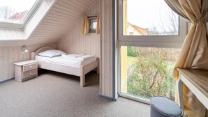 Quarto com teto inclinado, claraboia, cama, mesa de cabeceira e janela com cortinas.