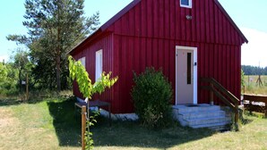 A red barn with a white door and a small window, surrounded by grass and trees. - Ferienhaus am Oase am Vilzsee (Mirow)