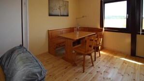 A room with a wooden dining table, chairs, a bench, a painting on the wall, and a window with a view. - Ferienhaus am Oase am Vilzsee (Mirow)