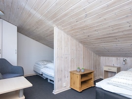 Un dormitorio con techo inclinado, una cama, un escritorio, una silla y un pequeño armario de madera.