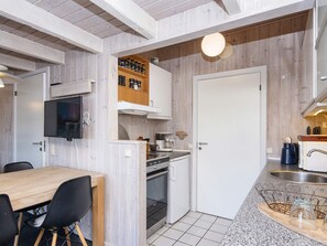 A compact kitchen with a dining area, wooden cabinets, a built-in oven, and a television mounted on the wall.
