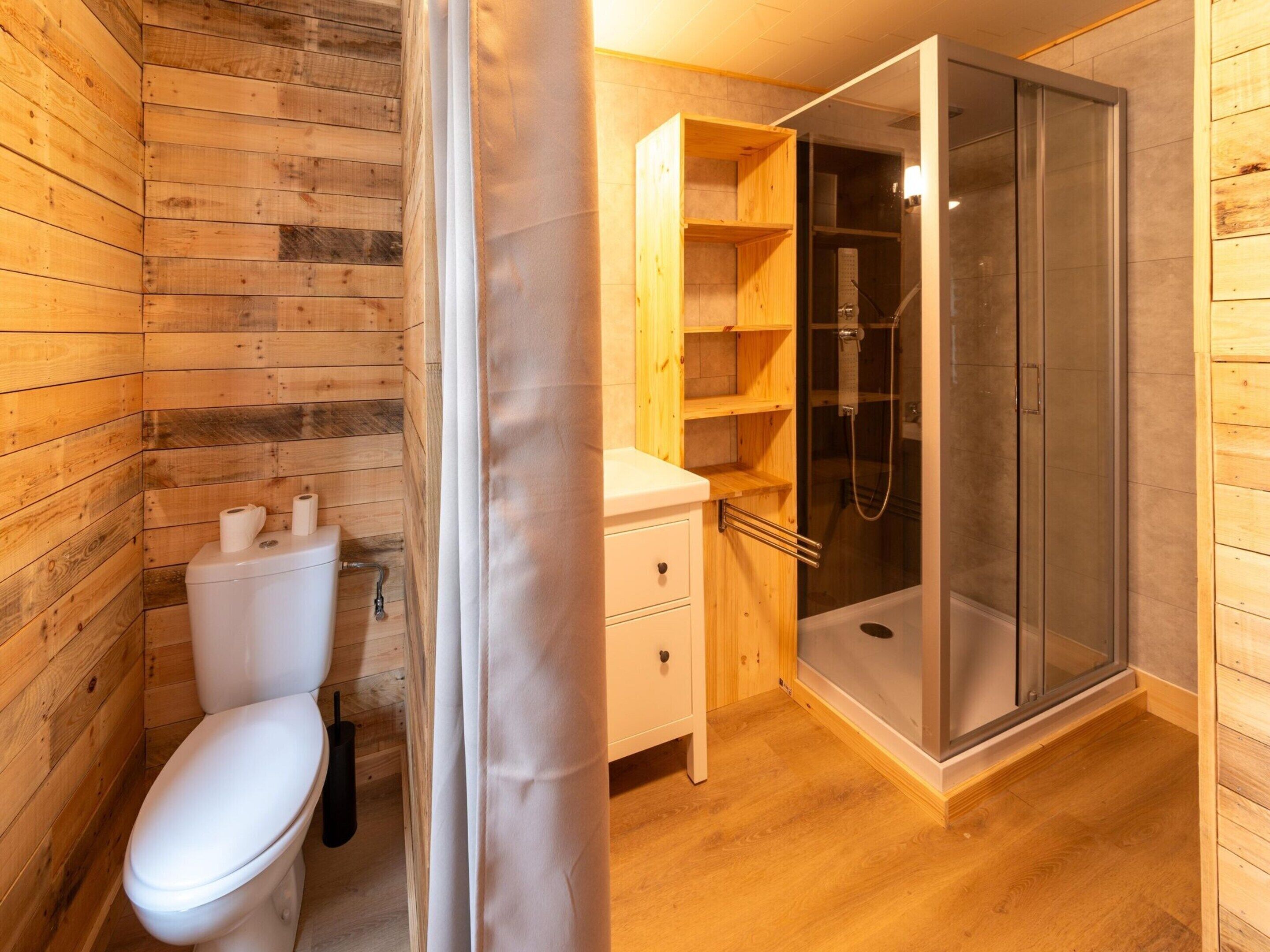 Een houten badkamer met een toilet, een douche en houten planken.
