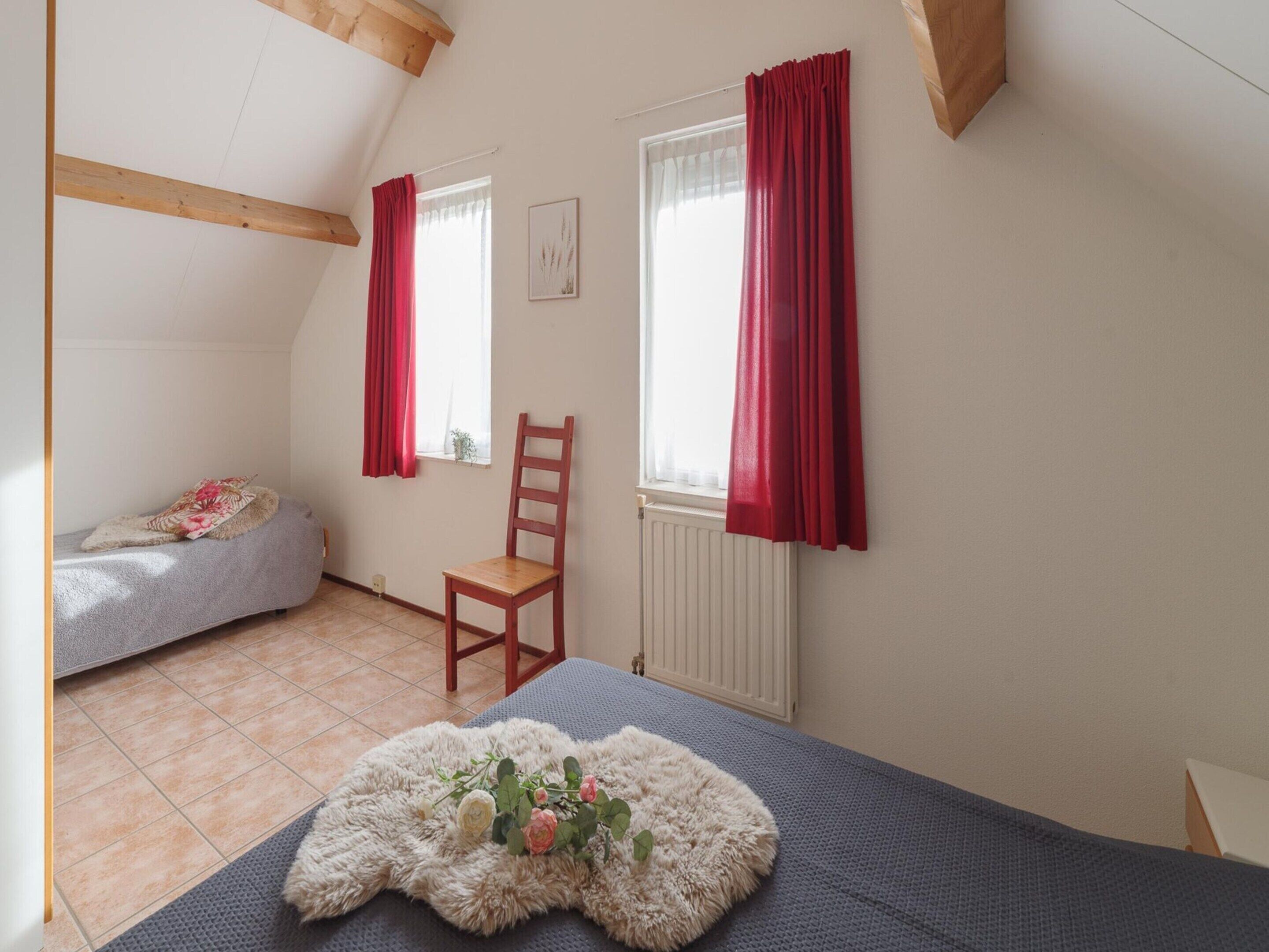 Une pièce avec un lit, une chaise, une fenêtre avec des rideaux rouges et un radiateur.